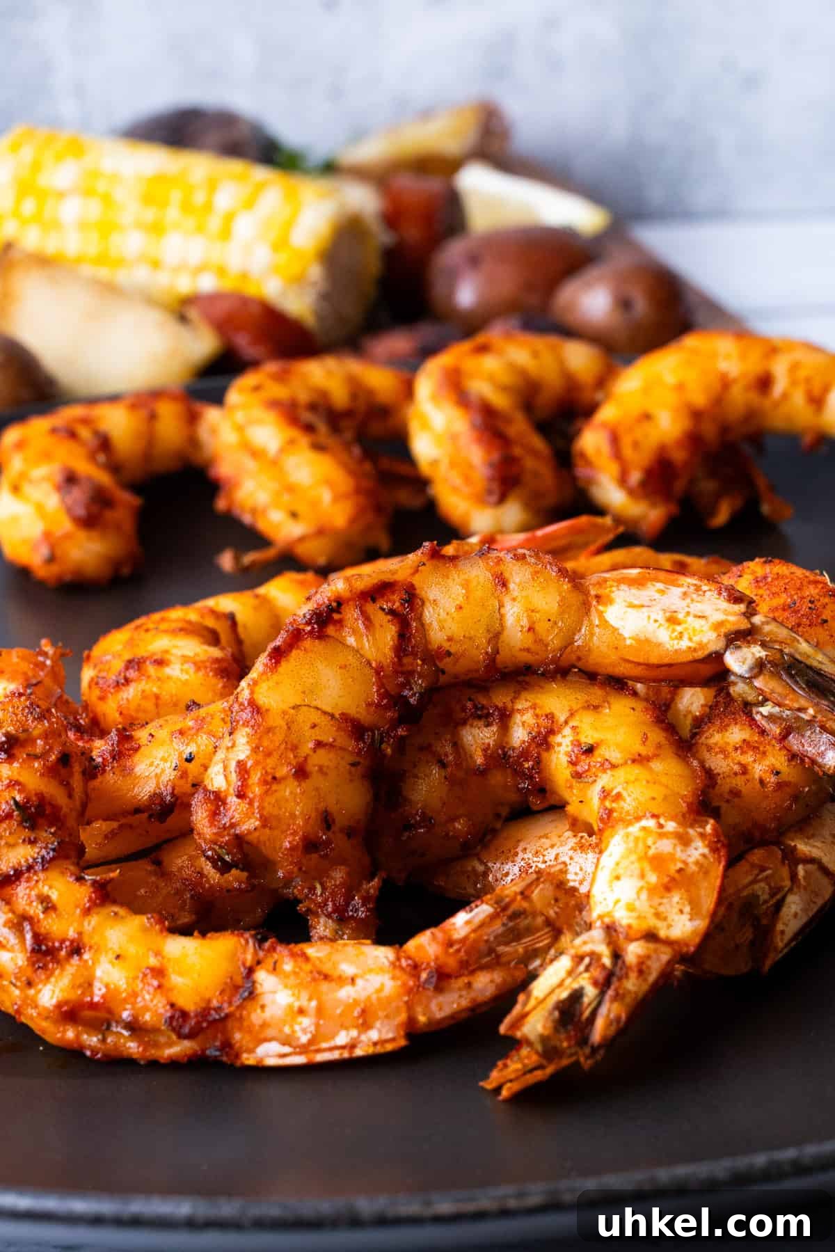 Smoked Shrimp Recipes: How to Smoke Shrimp Perfectly 14 Smoked shrimp on black plate with corn on the cob in background.