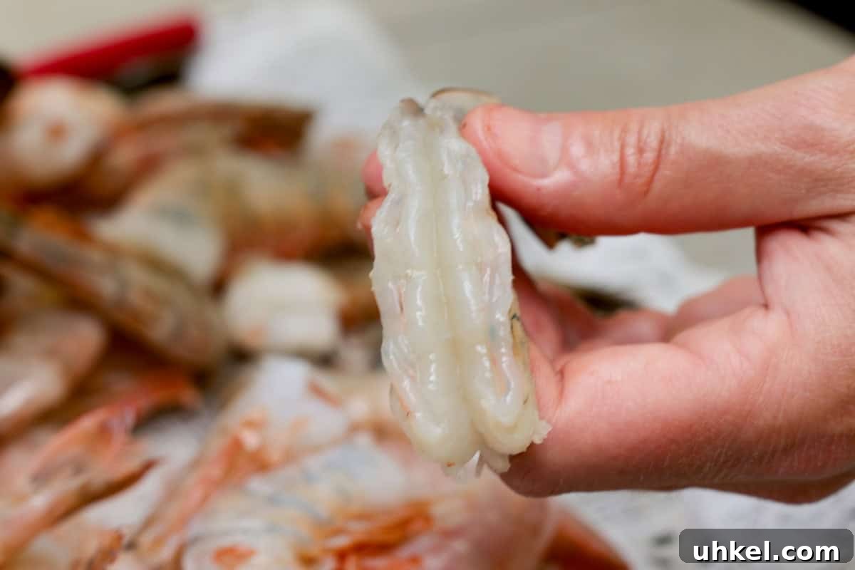Smoked Shrimp Recipes: How to Smoke Shrimp Perfectly 6 Holding a deveined and rinsed shrimp in hand with plate of shrimp in background.