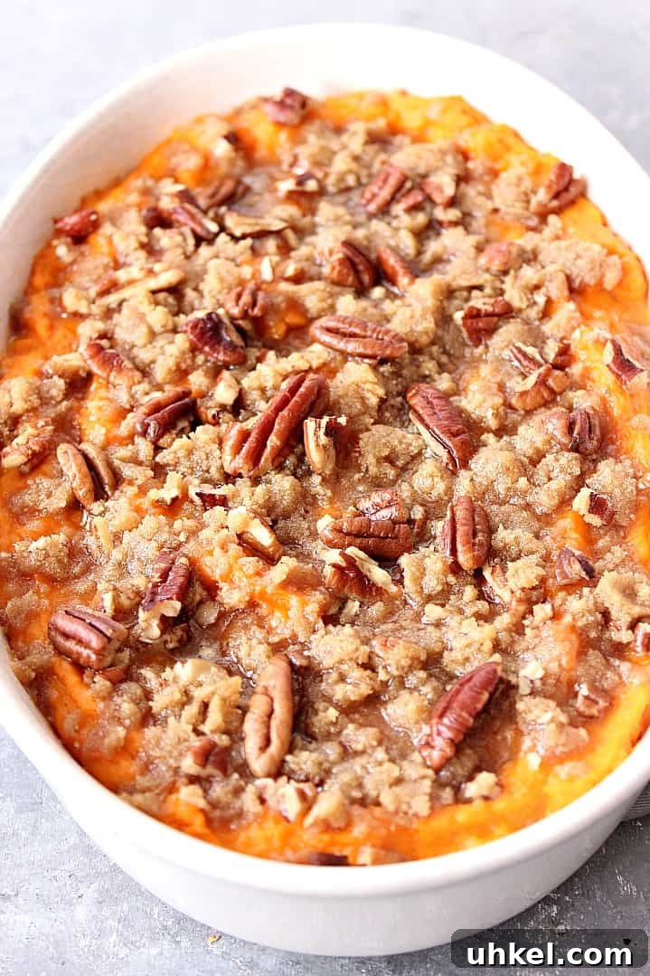 The Best Easy Sweet Potato Casserole Recipe Close up shot of baked sweet potato casserole, topped with pecans and brown sugar.
