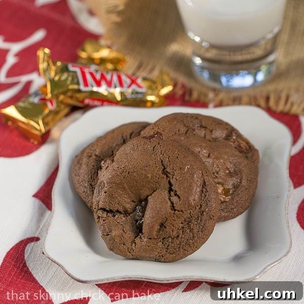 Double Chocolate Twix Cookies - rich, chocolate cookies filled with chunks of decadent Twix bars! Three Double Chocolate Twix Cookies on a square white plate