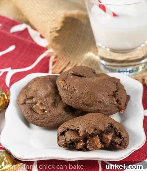 Double Chocolate Twix Cookies - rich, chocolate cookies filled with chunks of decadent Twix bars! Double Chocolate Twix Cookies on a white plate with one broken open to reveal the candy filled interior