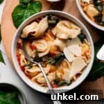 A bowl with tortellini and wilted spinach in a tomato broth garnished with parmesan cheese.