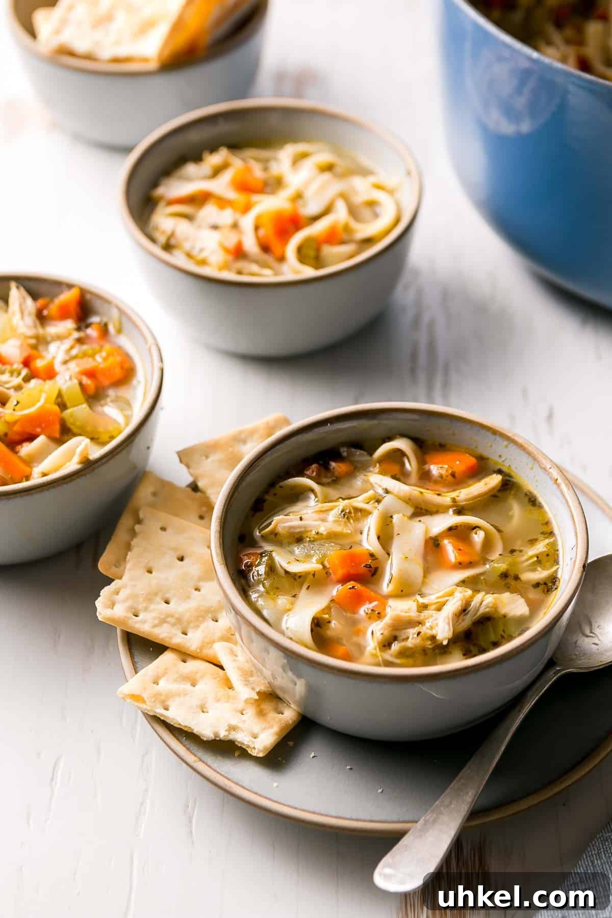 Three bowls of gluten free chicken noodle soup, one with crackers to the side.