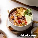 Bowl of chicken tortilla soup garnished with tortilla chips, lime wedges, and cilantro.