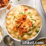 Gluten-free potato soup in a cream bowl topped with chives and bacon next to a pot of the soup.