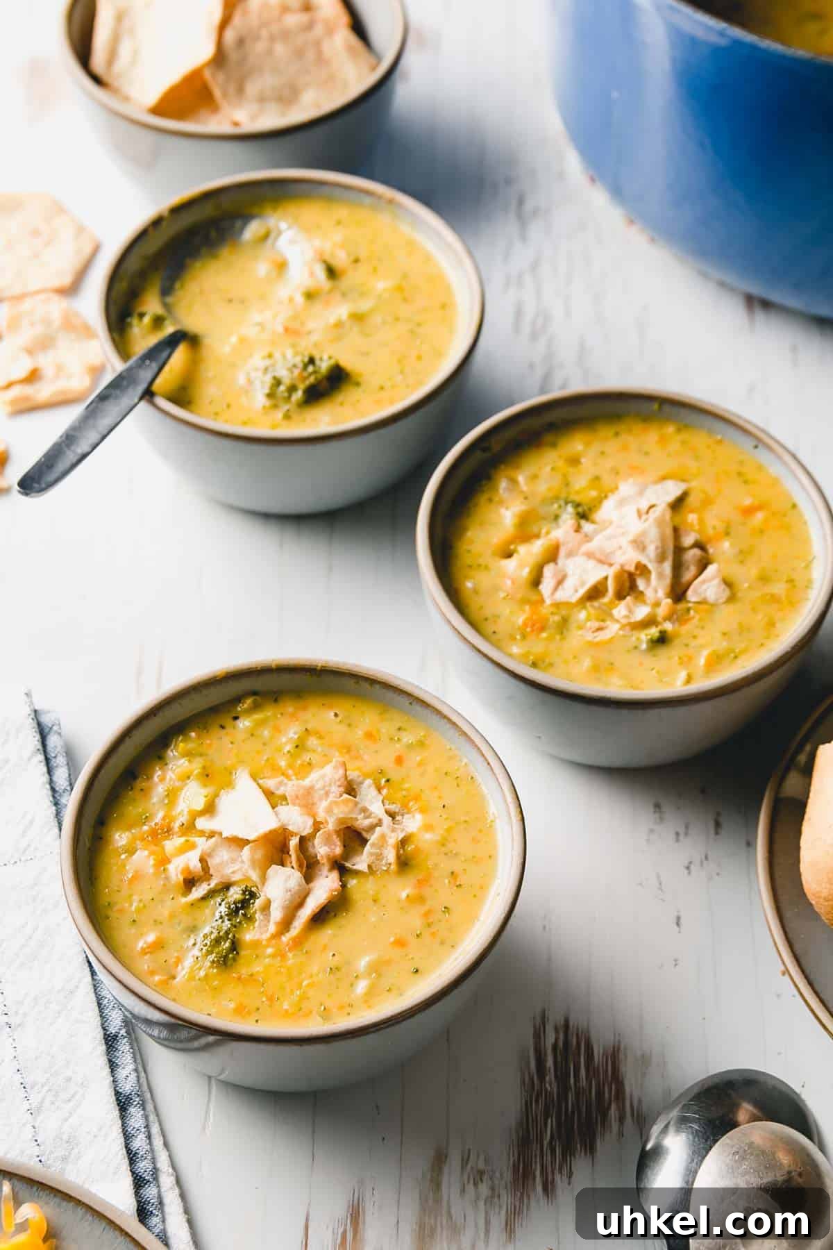 Three bowls of gluten free broccoli cheddar soup. Blue pot in background.