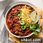A bowl of chili garnished with cheese, jalapenos, green onion, and lime wedges.