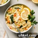 Gluten free lemon chicken orzo soup in a bowl with lemons slices and parsley for garnish.