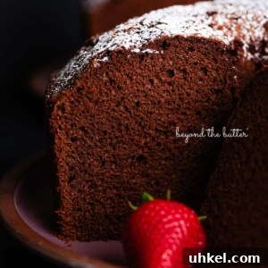 Moist Chocolate Chiffon Cake Recipe for Light, Fluffy Dessert 11 Chocolate chiffon cake sliced with whole strawberries placed on and in front of a dark purple ceramic plate on a black background.