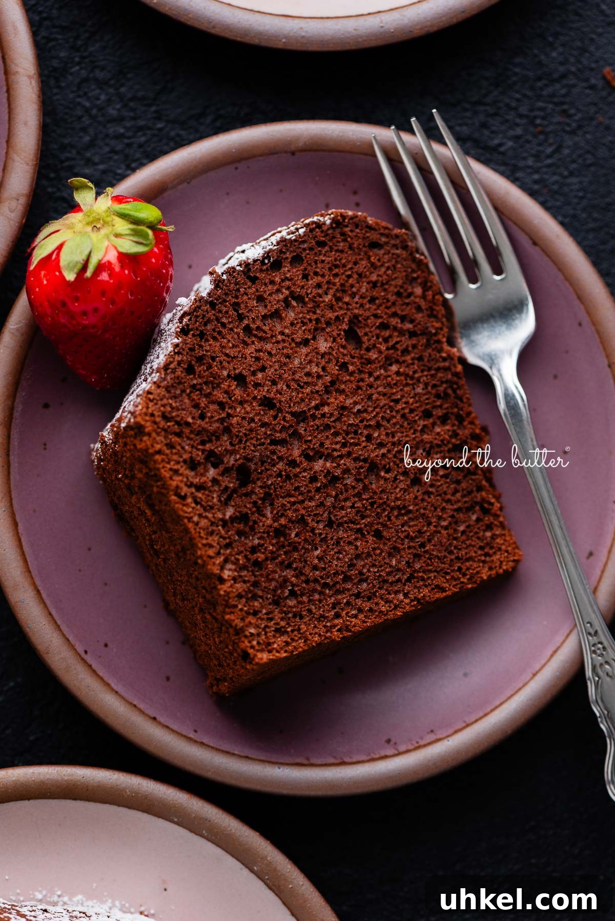 Moist Chocolate Chiffon Cake Recipe for Light, Fluffy Dessert 10 Slices of chocolate chiffon cake on small dark purple and light pink ceramic dessert plates with a fork and strawberry placed on each one on a black background.