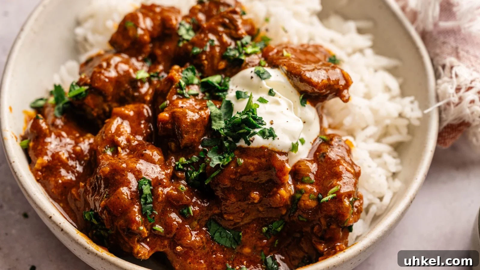 23 Spring Dinner Recipes to Lighten Up Heavy Weeknight Meals 13 A bowl of white rice topped with chunks of beef in a reddish-brown sauce, garnished with fresh herbs and a dollop of cream.