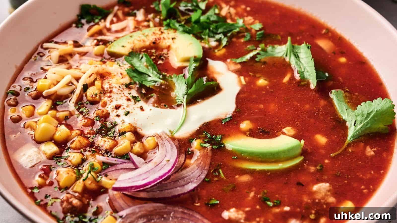 23 Spring Dinner Recipes to Lighten Up Heavy Weeknight Meals 14 A bowl of red soup topped with avocado slices, sour cream, cilantro, sliced onions, corn, and shredded cheese.