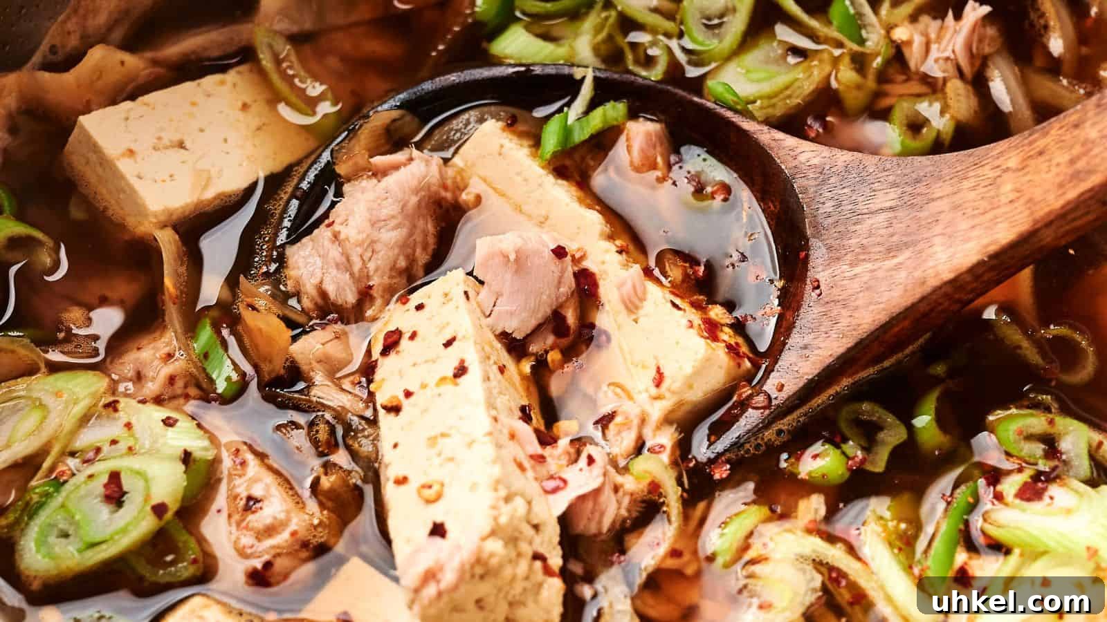23 Spring Dinner Recipes to Lighten Up Heavy Weeknight Meals 4 Close-up of a wooden spoon in a vibrant kimchi stew with tofu and pork, garnished with sliced green onions and red pepper flakes.