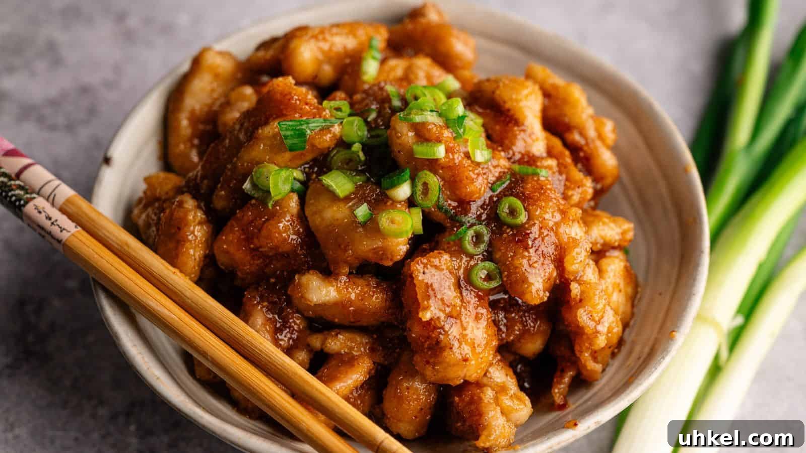 23 Spring Dinner Recipes to Lighten Up Heavy Weeknight Meals 8 A bowl of glazed chicken pieces topped with chopped green onions, with chopsticks resting on the bowl and green onions beside it.
