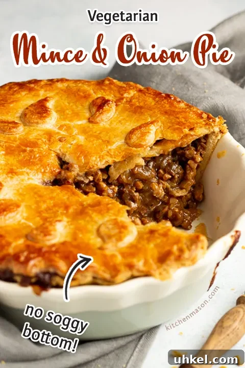 A baked vegetarian mince and onion pie with a slice cut out, decorated with pastry leaves, sat on a grey linen napkin with a wooden handled fork. Set on a pale blue wash backdrop.