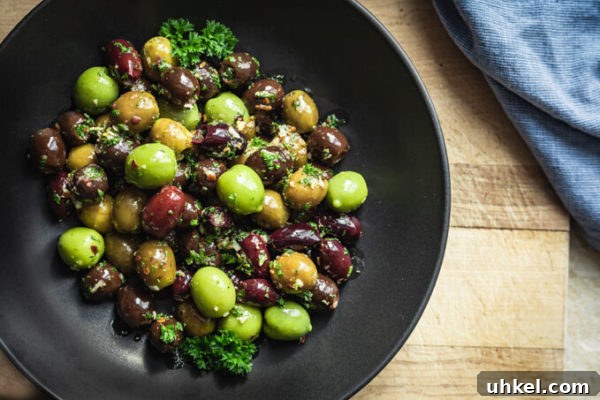 Green and black marinated olives with herbs, spices, garlic, oil and vinegar with parsley in a black bowl