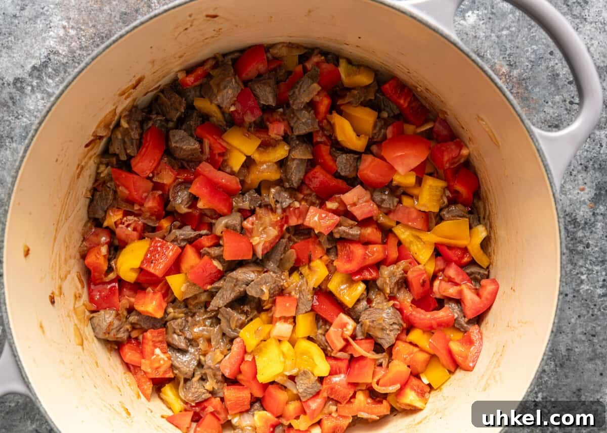 Traditional Hungarian Goulash Recipe: Hearty Beef Stew Guide 7 overhead process shot: peppers and tomatoes added to beef cubes