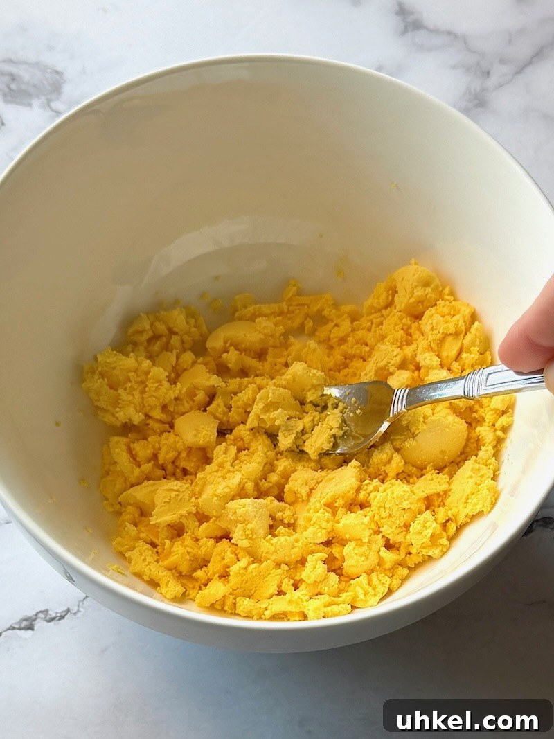 Classic Deviled Eggs Recipe for Gatherings 10 A fork smashing the cooked egg yolks in a bowl.