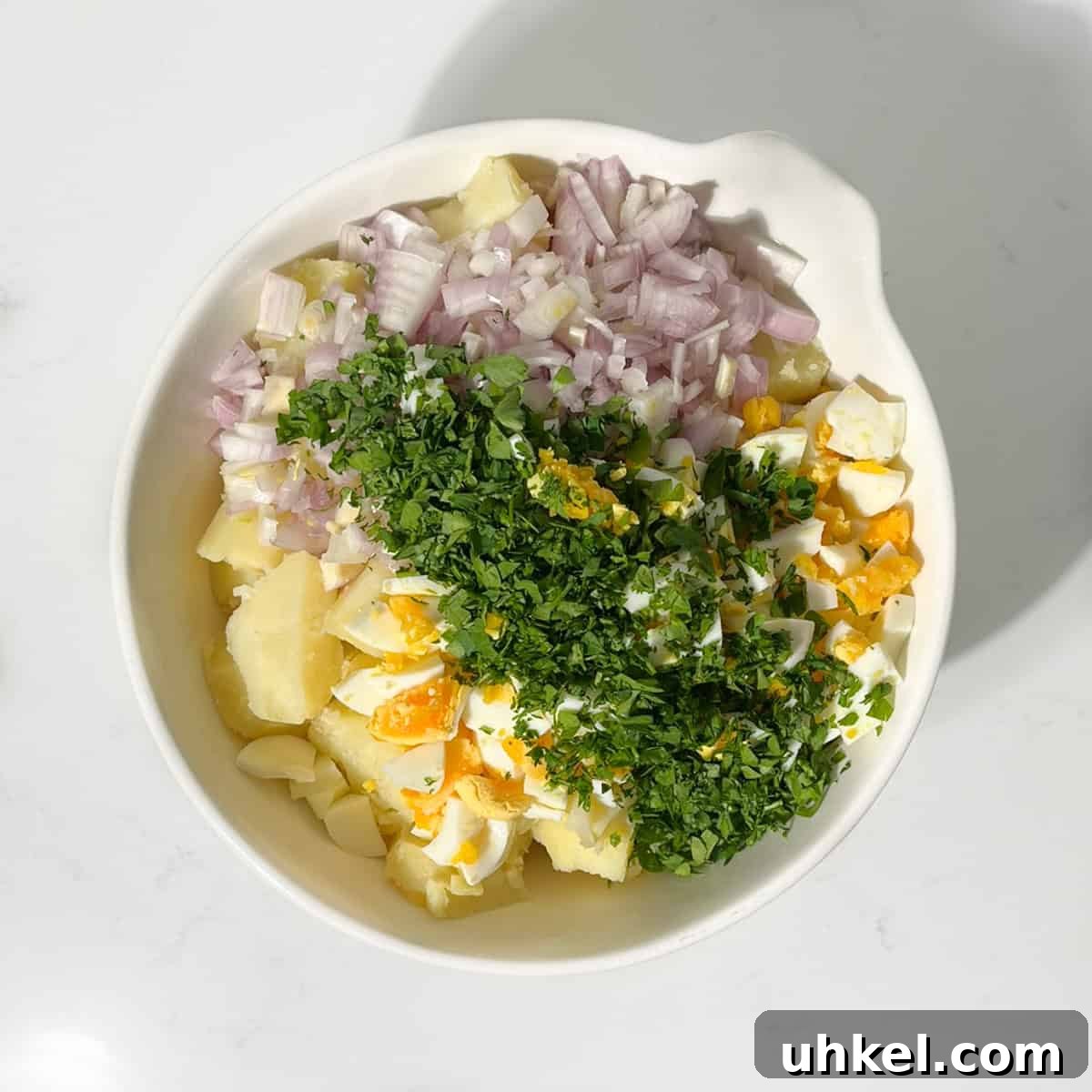 Creamy Potato Salad with Sweetened Condensed Milk Recipe 7 Adding the herbs, boiled eggs and onion to the sliced potato in a large white bowl.