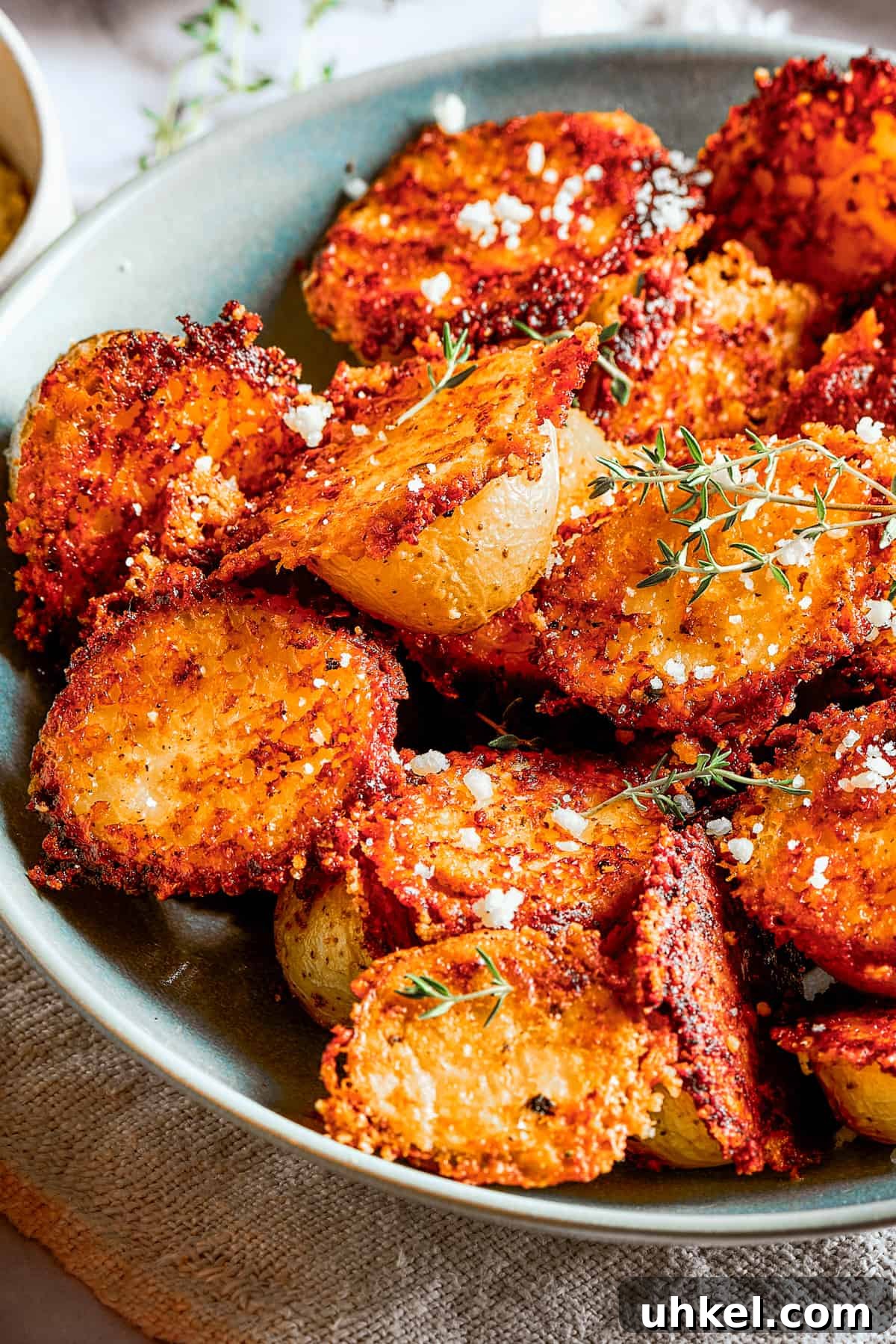 These tender potatoes with a crunchy, cheesy crust are the easiest, tastiest side dish you'll ever make. A viral TikTok recipe you'll love! Cheesy roasted potatoes in a bowl next to cups of dipping sauce, a cloth napkin, and a serving on a plate.