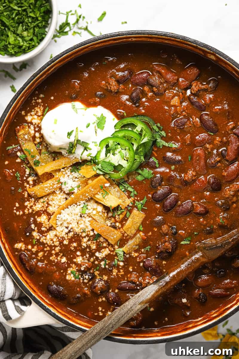 Large white pot filled with beer chili garnished with cilantro and tortilla strips