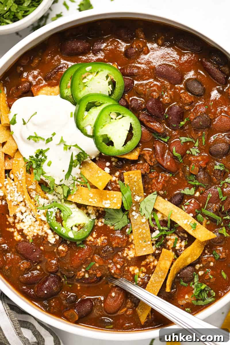 White bowl filled with beer chili garnished with cilantro and tortilla strips