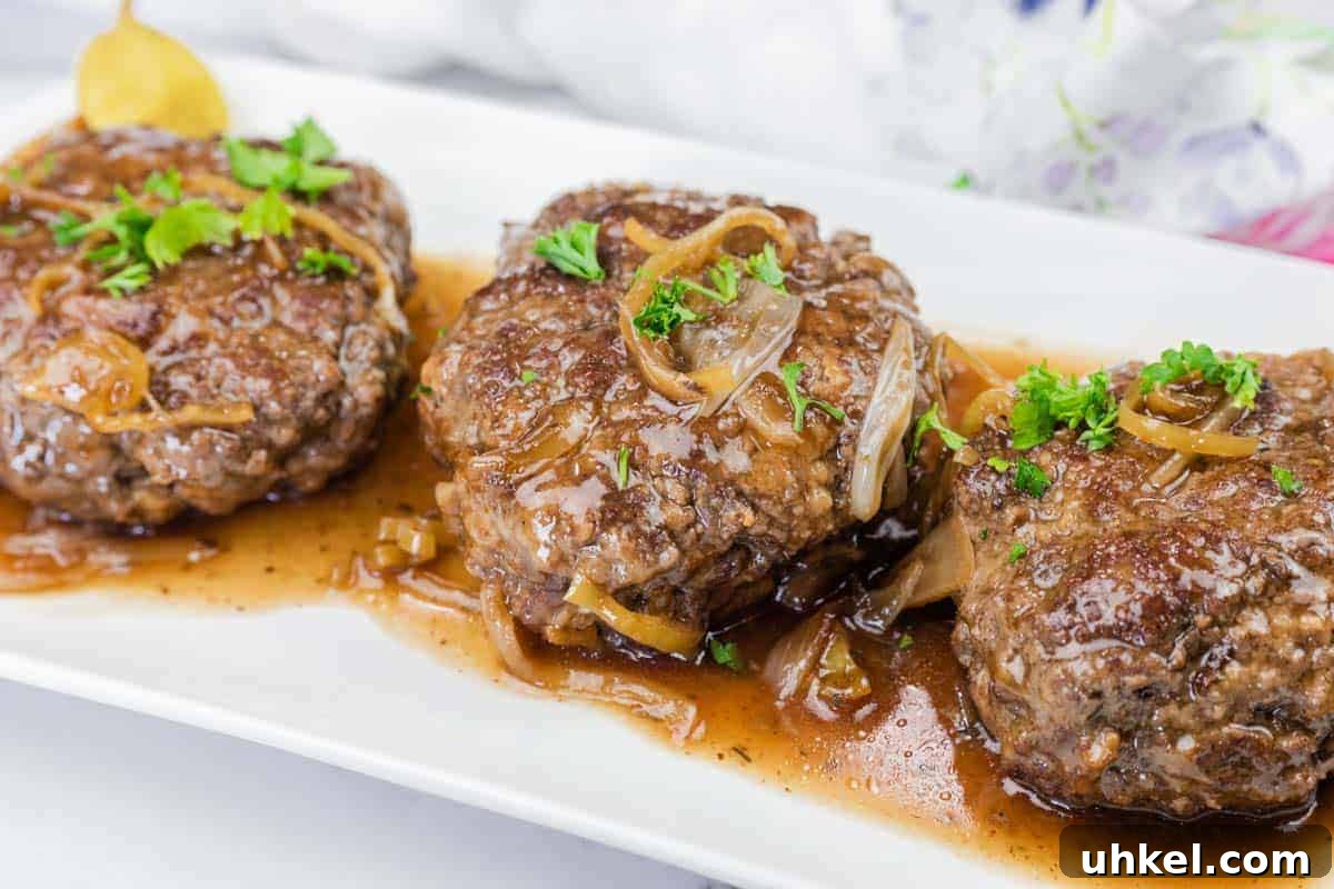 35 Timeless Southern Recipes That Always Delight 11 Three Mississippi Salisbury Steak covered in brown onion gravy, garnished with chopped parsley, served on a white rectangular plate.