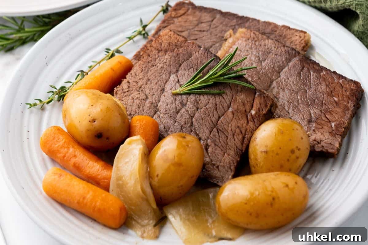 35 Timeless Southern Recipes That Always Delight 14 A plate of slow cooker rump roast with potatoes, carrots, onions, and a sprig of rosemary on a white dish.