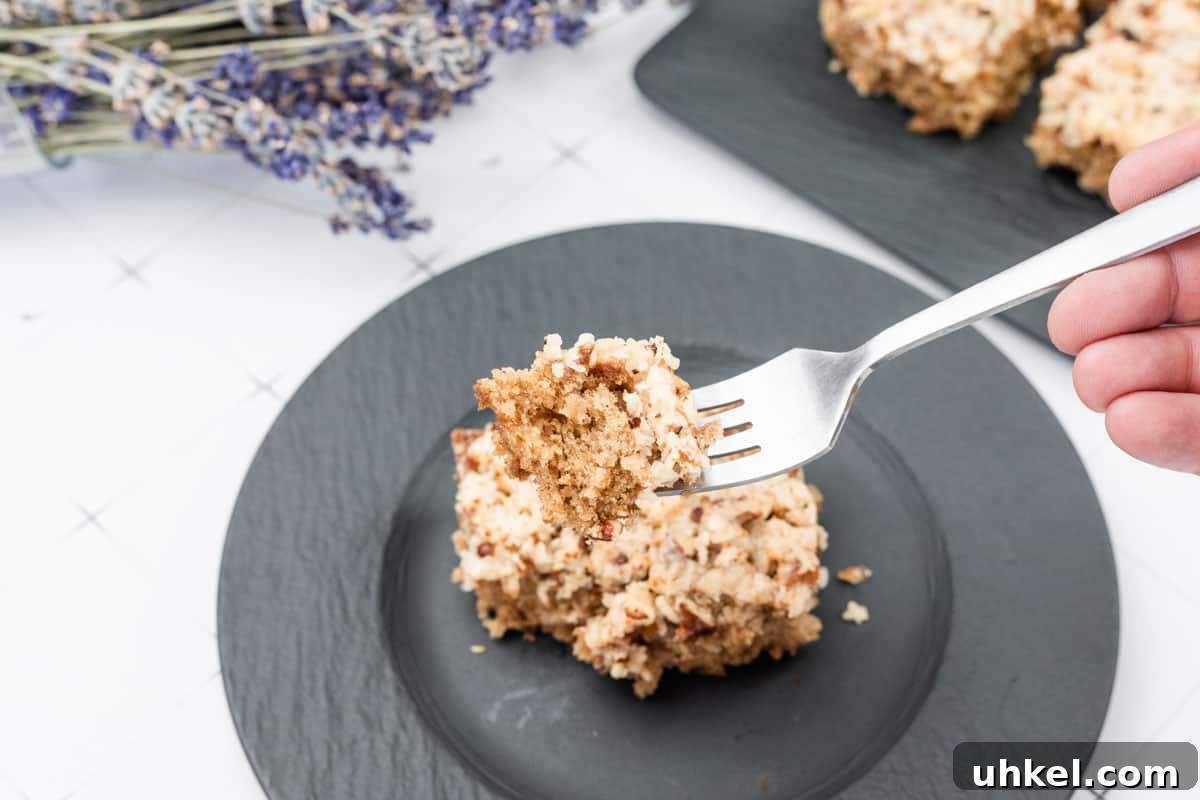 35 Timeless Southern Recipes That Always Delight 18 A fork holds a bite of Old Fashioned Lazy Daisy Oatmeal Cake above a black plate with more cake pieces, with dried lavender in the background.
