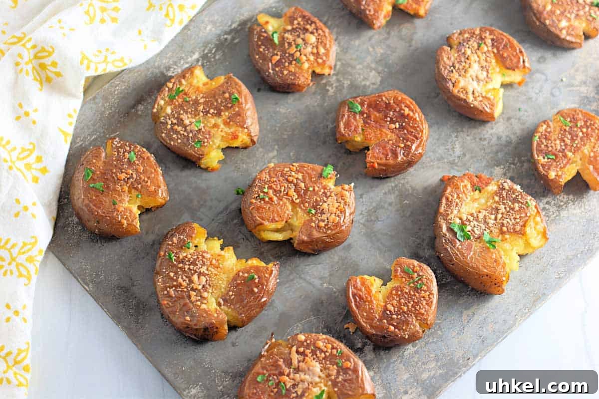 35 Timeless Southern Recipes That Always Delight 23 A baking sheet with several smashed roasted potatoes, garnished with herbs and grated cheese, arranged in rows.