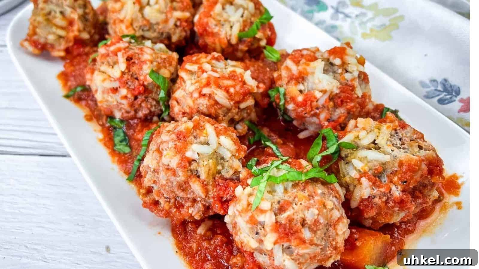 35 Timeless Southern Recipes That Always Delight 24 A white rectangular plate with several meatballs covered in tomato sauce, garnished with chopped basil.