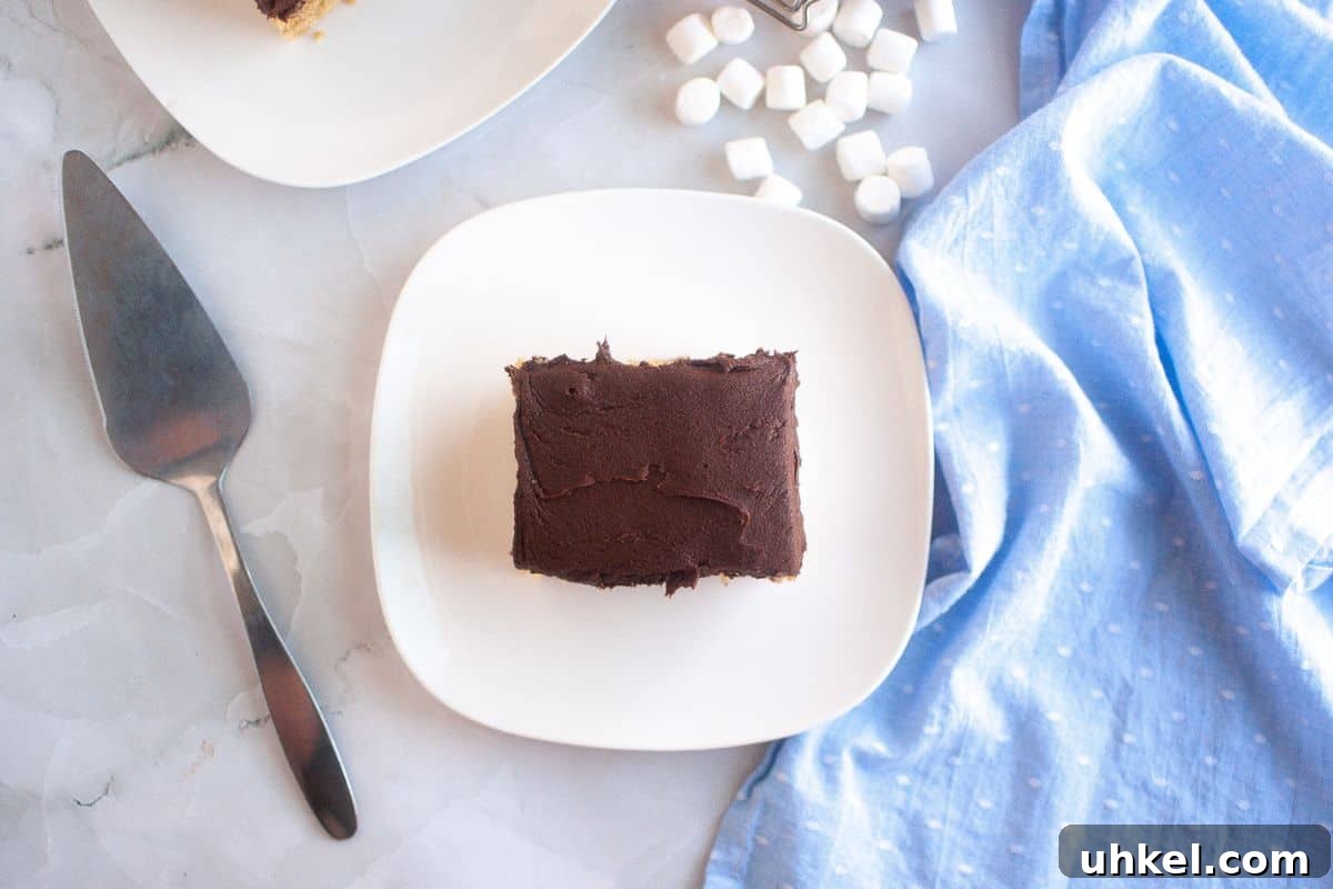 35 Timeless Southern Recipes That Always Delight 28 A square slice of Graham Cracker Cake on a white plate, with a cake server, blue cloth, and mini marshmallows nearby.
