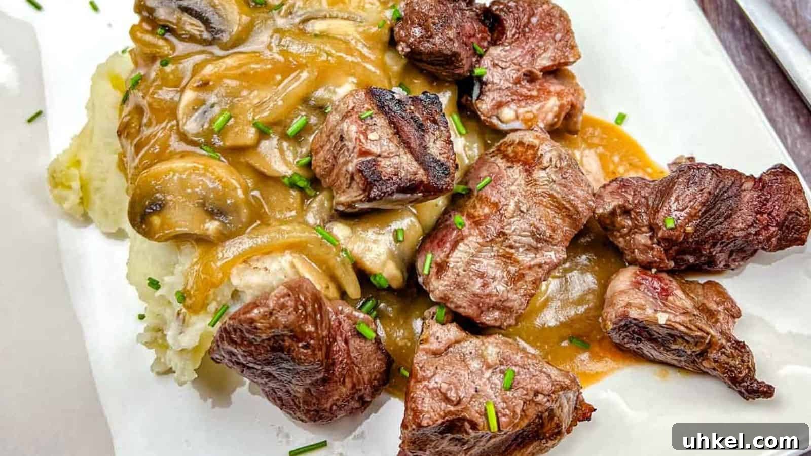 35 Timeless Southern Recipes That Always Delight 30 Texas Roadhouse Beef Tips with mushroom gravy over mashed potatoes, garnished with chives on a white plate.