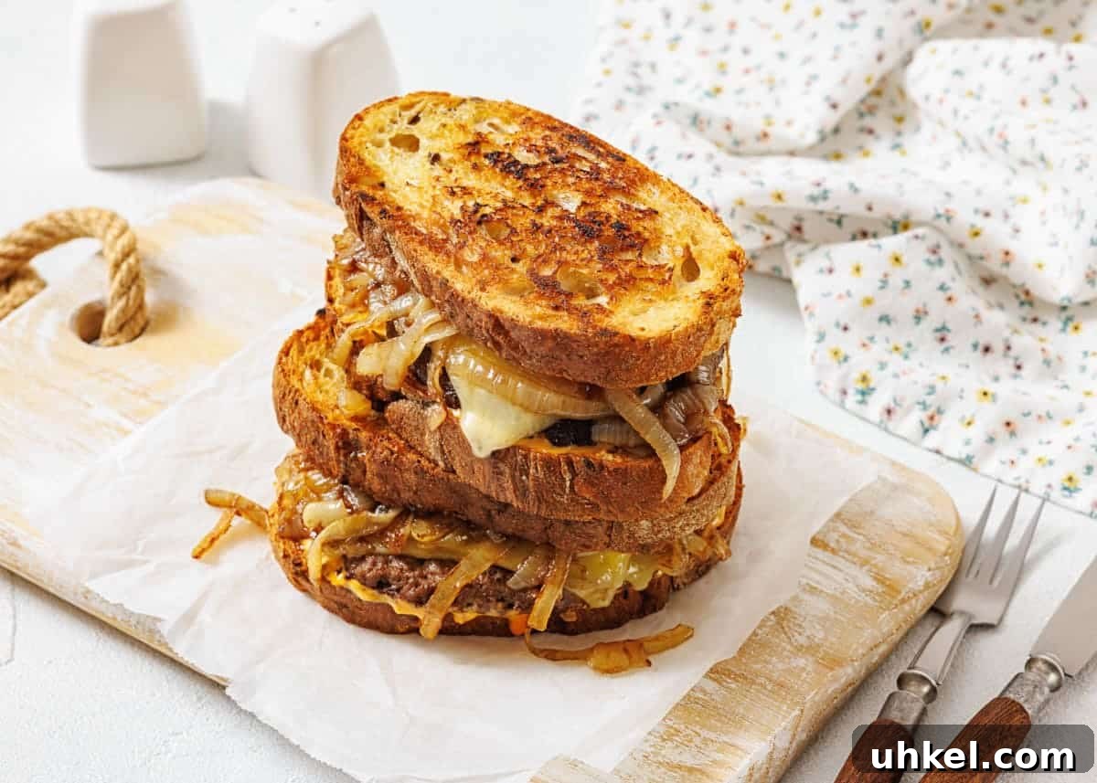 35 Timeless Southern Recipes That Always Delight 4 A stack of two patty melt sandwiches with caramelized onions and melted cheese on toasted bread, placed on parchment paper atop a wooden board.