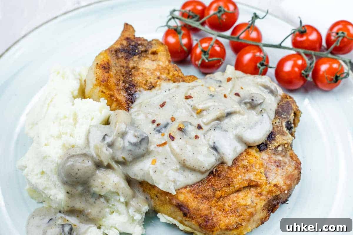 35 Timeless Southern Recipes That Always Delight 5 Plate with Cast Iron Smothered Pork Chops served alongside mashed potatoes and vine tomatoes.