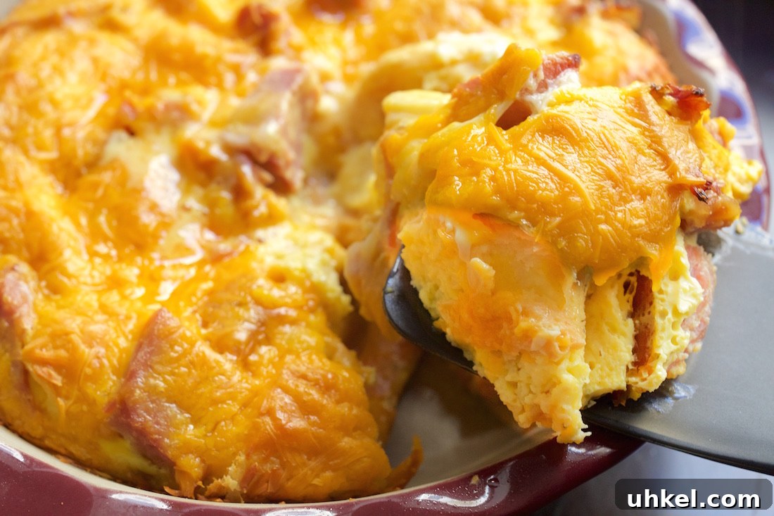 Ham and Cheese Croissant Casserole: Quick Savory Breakfast Bake 3 A spatula holds up a piece of ham and croissant breakfast casserole with the casserole dish in the background