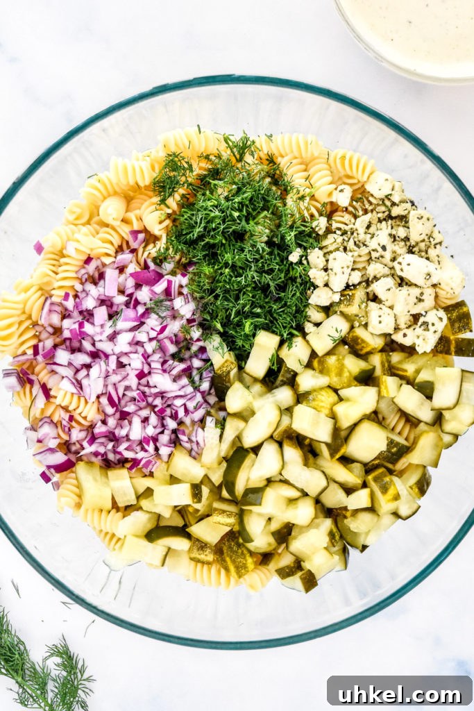 Creamy Dill Pickle Pasta Salad Recipe for Summer Potlucks 6 pickles, red onion, dill, feta and cooked pasta in a large bowl.