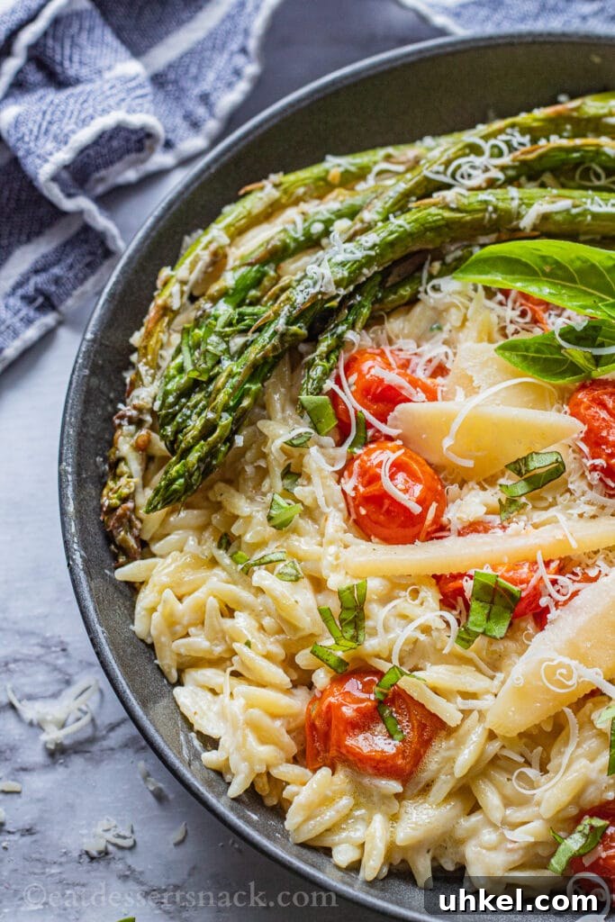Creamy Orzo with Oven-Roasted Asparagus and Parmesan 2 Black pan of cooked orzo, roasted asparagus and tomatoes, parmesan cheese on top with blue tea towel.