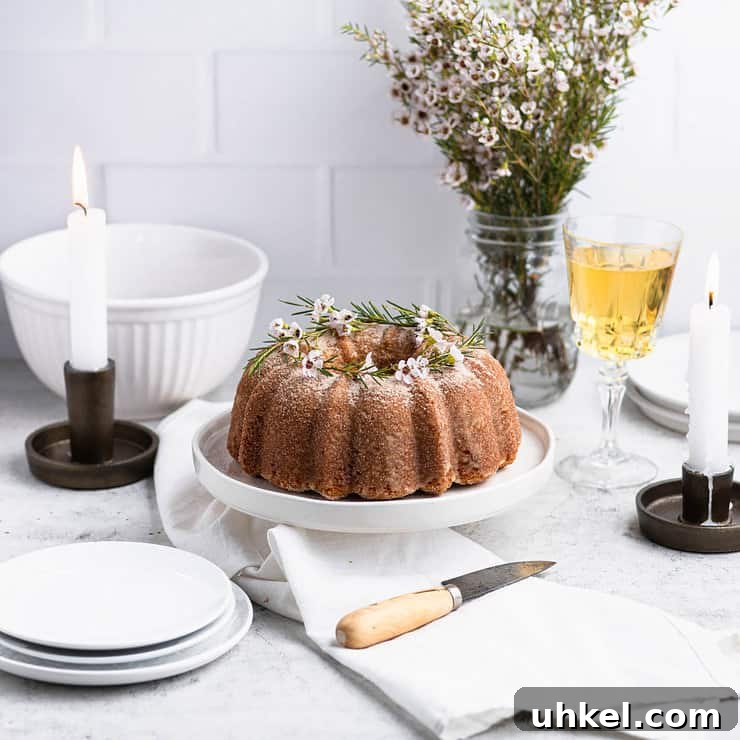 Top Fall Cakes to Bake This Season 3 Apple cider donut bundt cake on a white cake stand with a white bowl, plates, candles and a glass of apple cider in the background.