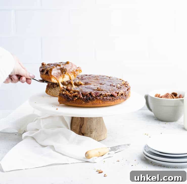 Top Fall Cakes to Bake This Season 4 slice being pulled from an pecan upside down cake with bits of caramel pulling between the slice and the rest of the cake with plates and a bowl of pecans in the background.