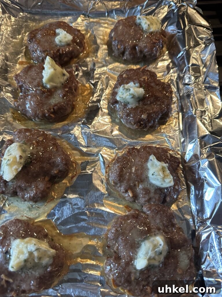 Spooky Onion Butter Burgers for Halloween Party Night 5 Cooked burger patties on a baking sheet with a dollop of butter mixture on each one.