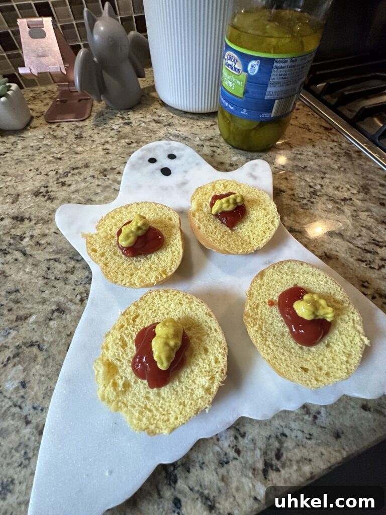 Spooky Onion Butter Burgers for Halloween Party Night 7 Four open faced buns with dollops of ketchup and mustard on a ghost shaped cutting board.