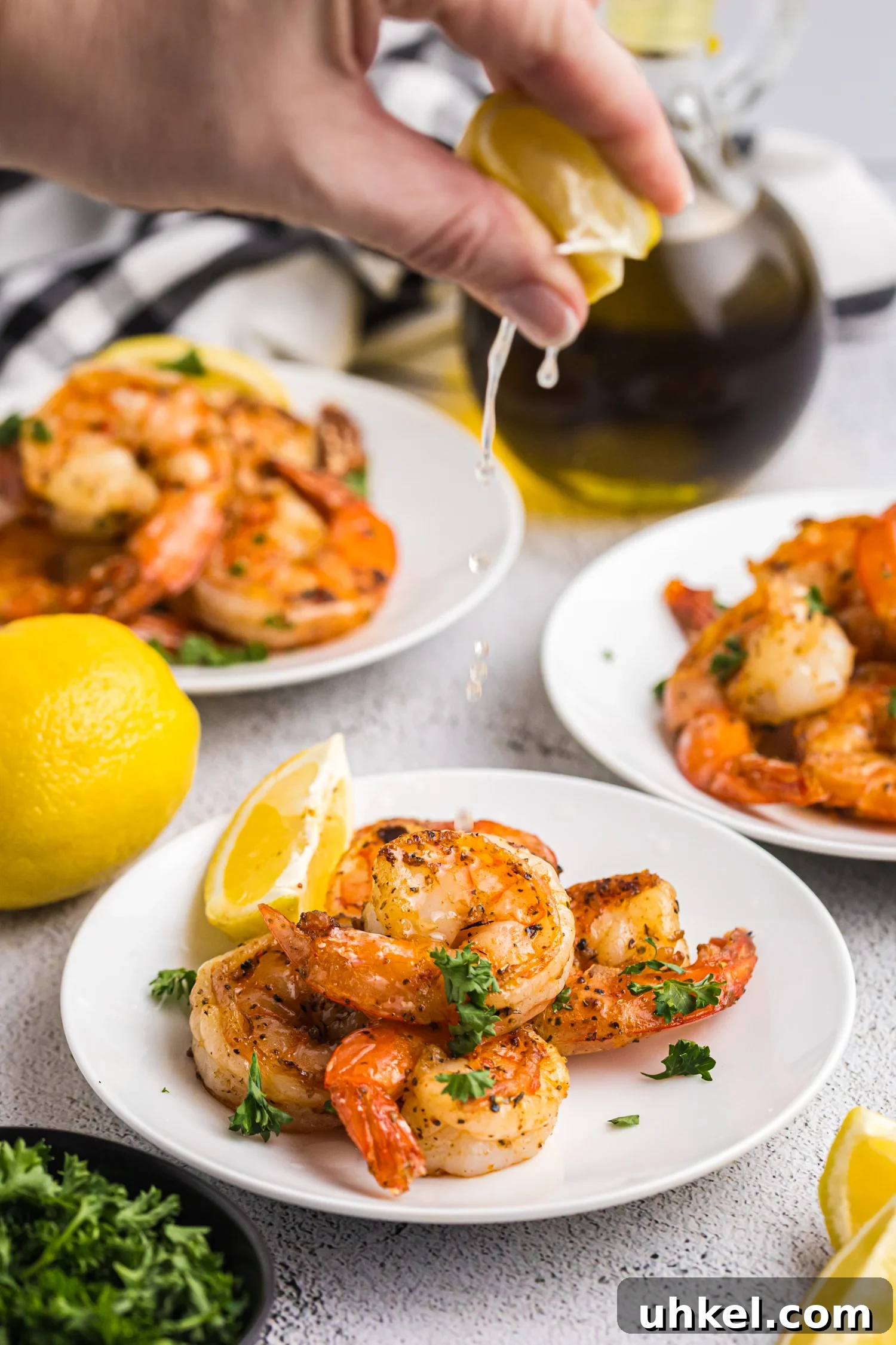 A hand squeezing fresh lemon juice over a plate of seasoned, grilled shrimp.