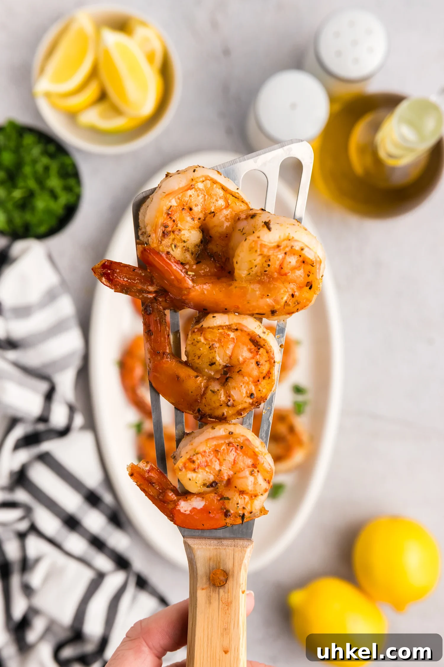 Cooked shrimp resting on a metal spatula held above a serving plate with parsley garnish.