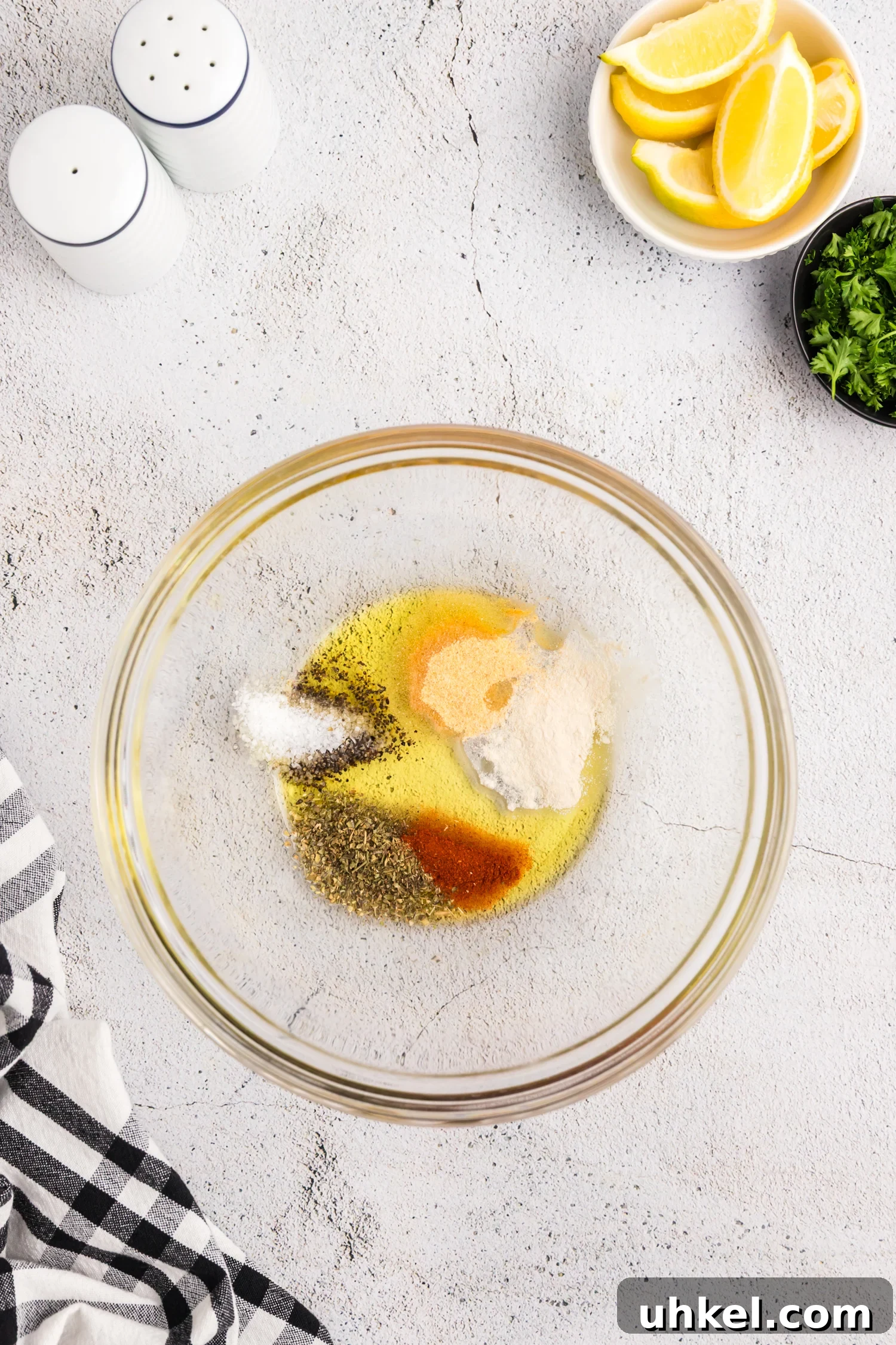 A glass bowl containing olive oil and a variety of seasonings, including paprika, salt, pepper, garlic powder, and herbs.