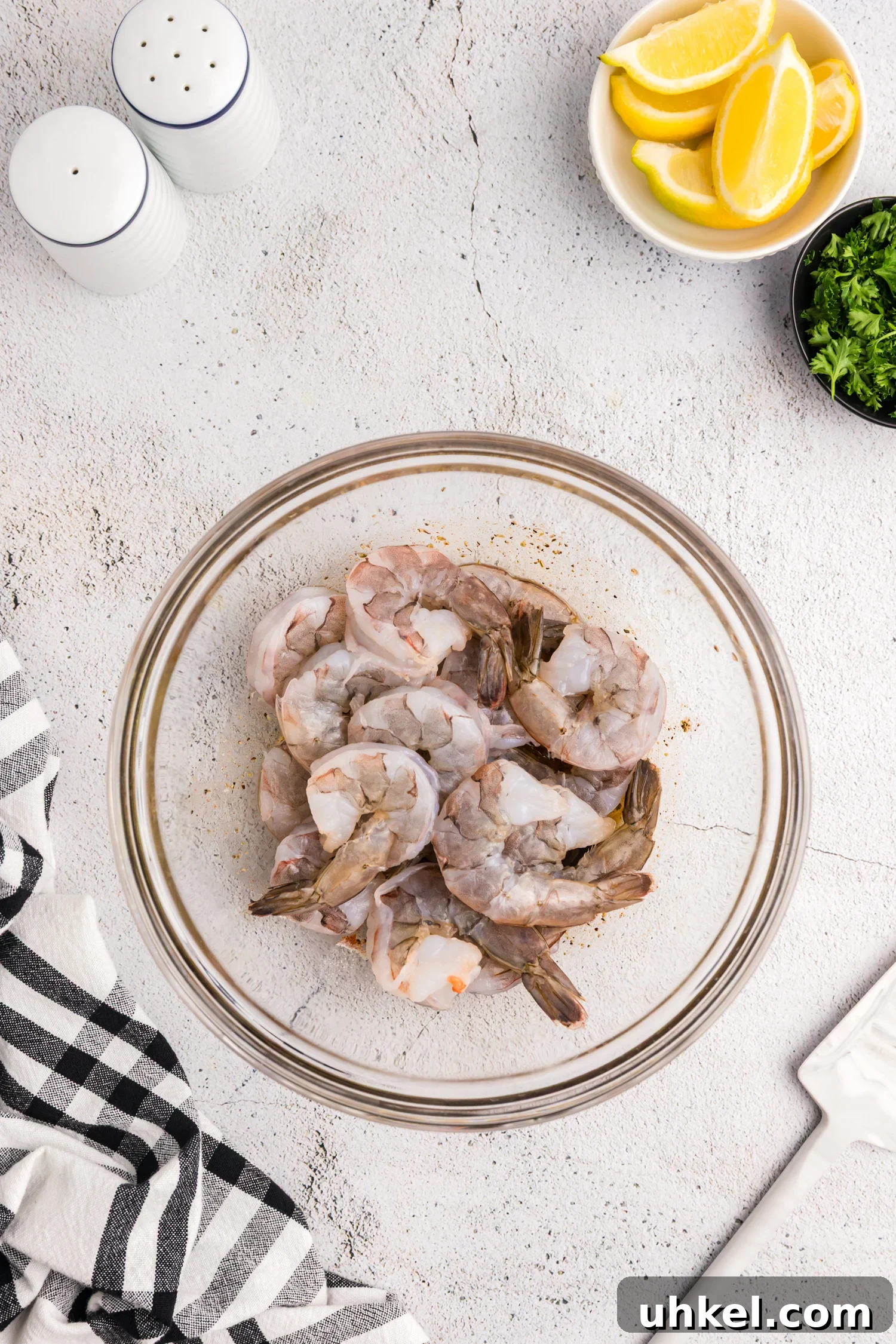 Raw shrimp added to a bowl with marinade at the bottom, about to be mixed.