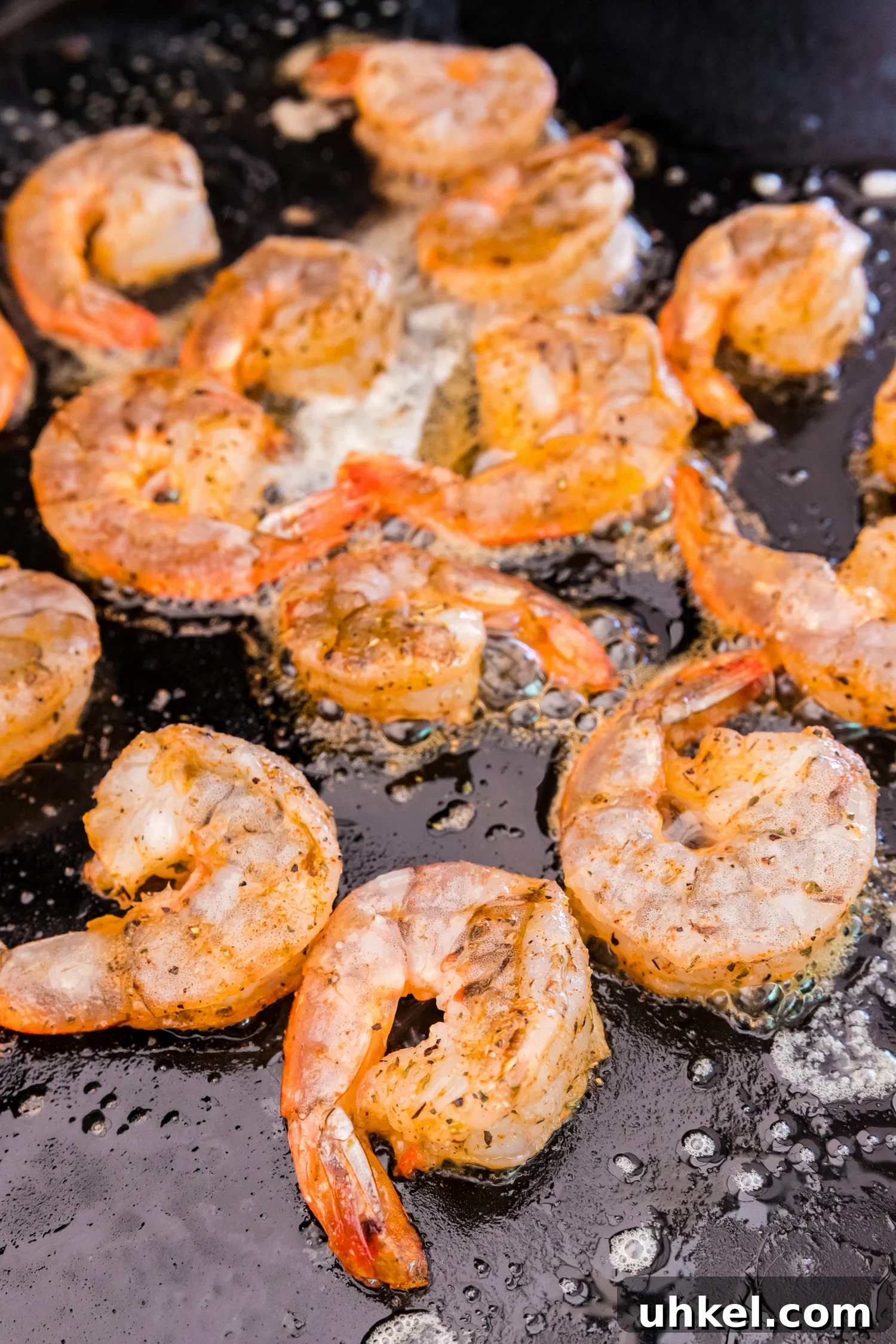 Shrimp sizzling on a hot griddle in melted butter, beginning to cook.