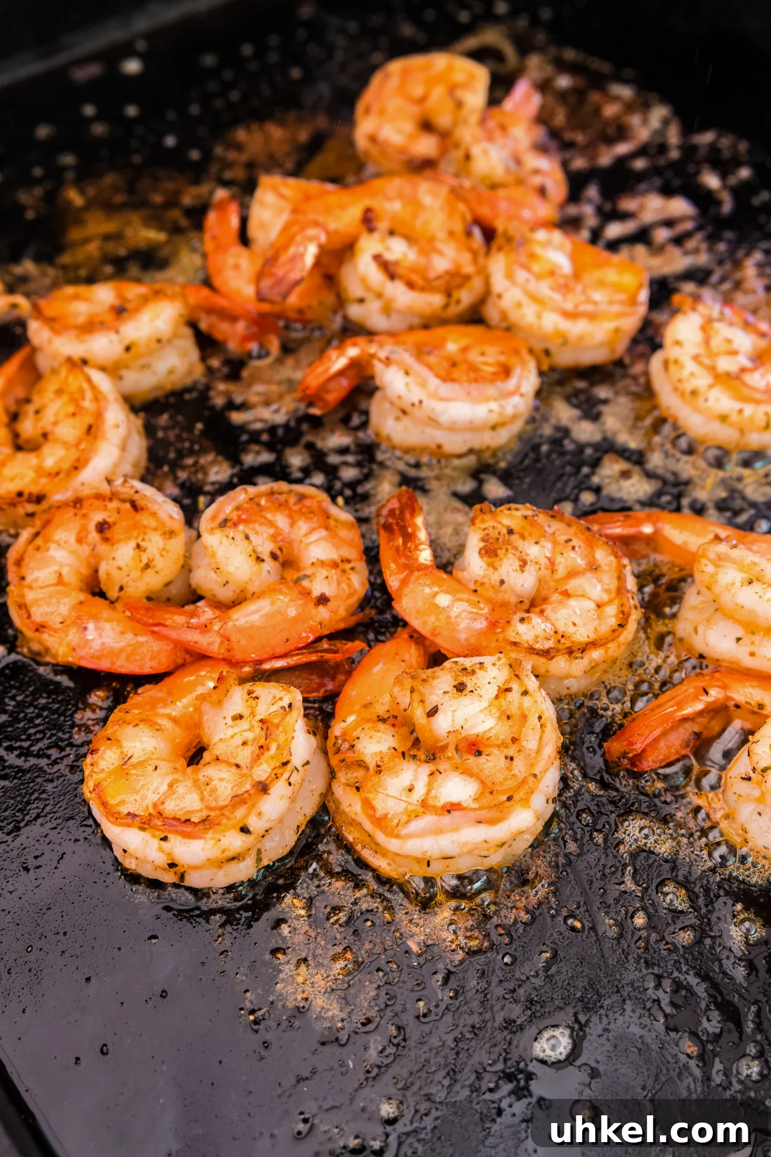 Close-up of shrimp on a flat-top griddle, fully cooked to a golden brown with slightly curled edges.