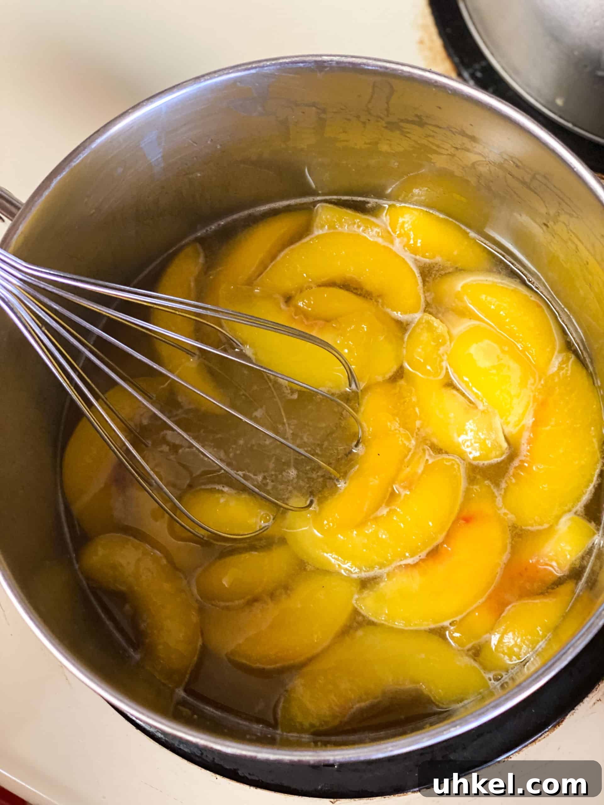 Homemade Peach Simple Syrup Recipe for Cocktails & Desserts 4 Peaches in sugar water being stirred with a whisk