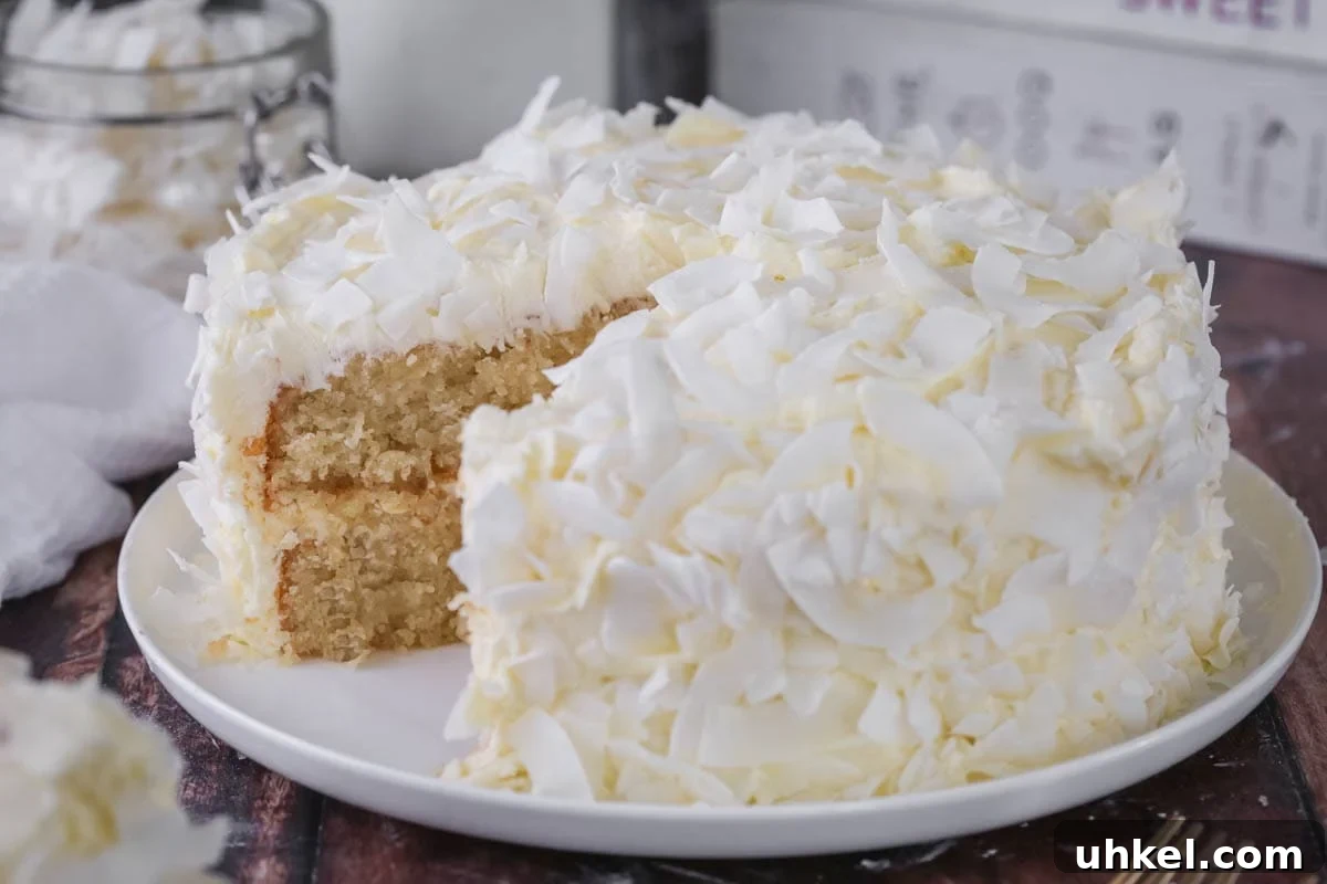 Coconut Cake Without Gluten: Moist Recipe for Allergy-Friendly Celebrations 18 Gluten-Free Coconut Cake covered in coconut flakes on a white plate. Cut into showing soft moisture texture.